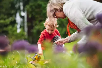 Elderly lady interacts with a young child in a garden.