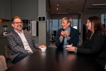 Three people talking at in an office dining area.